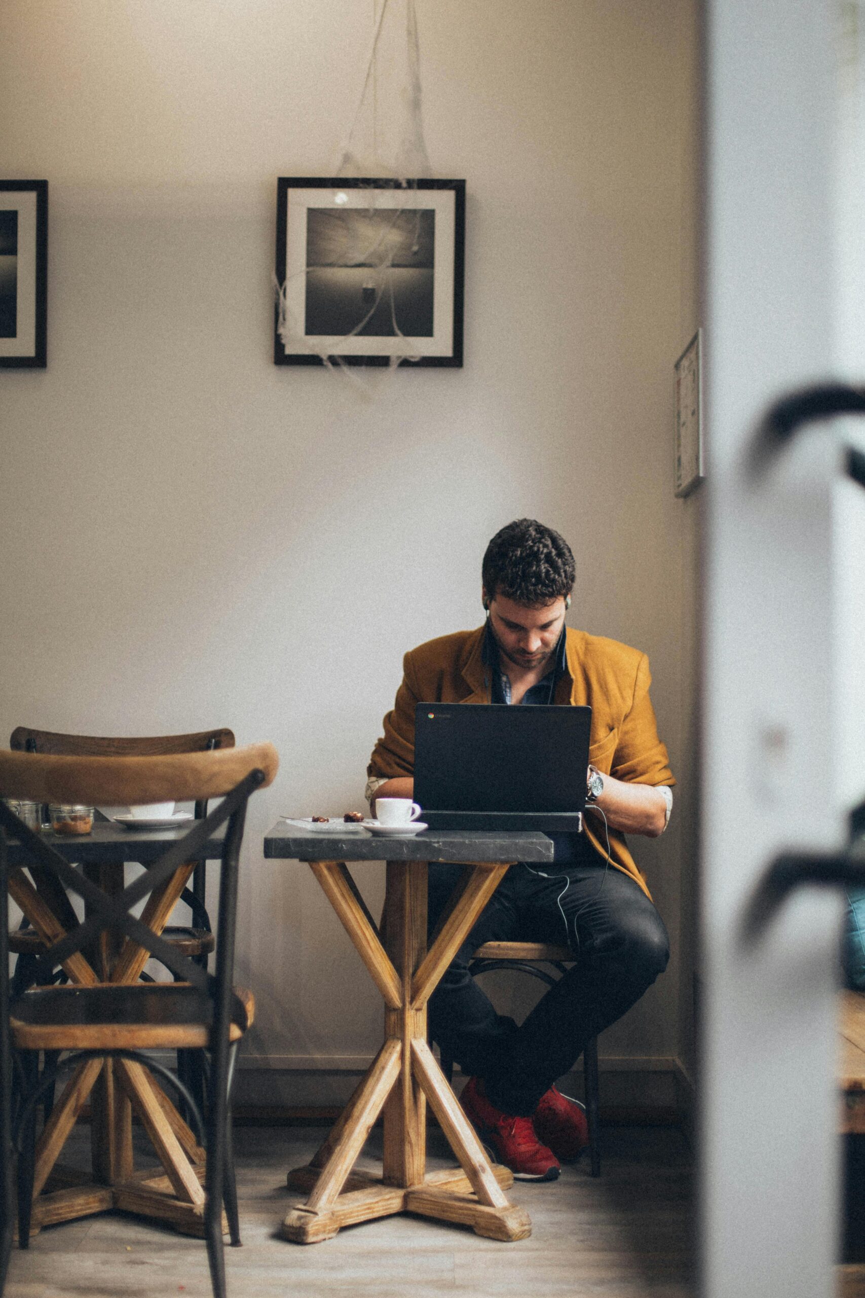 A man wearing a jacket is focused on his laptop in a cozy café interior.